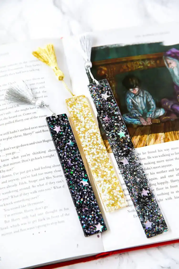 Several elegant resin bookmarks with embedded gold flakes and dried botanicals, topped with silk tassels.