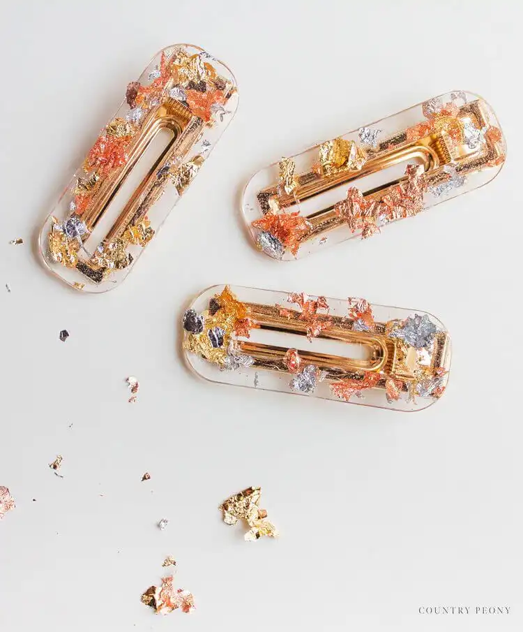 Shiny metallic foil resin hair barrettes in various shapes, reflecting light and showing embedded gold and silver flakes.