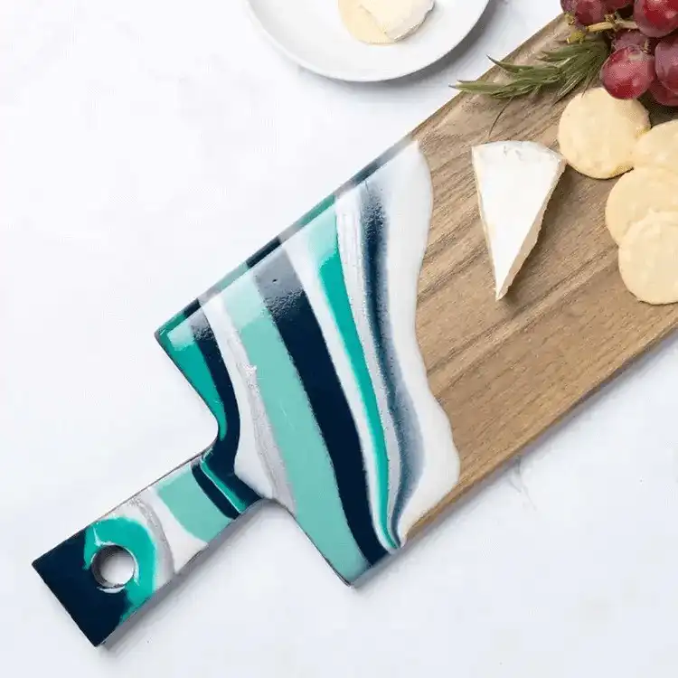 A wooden cutting board with a beautiful blue and white marbled resin section, suitable for serving.