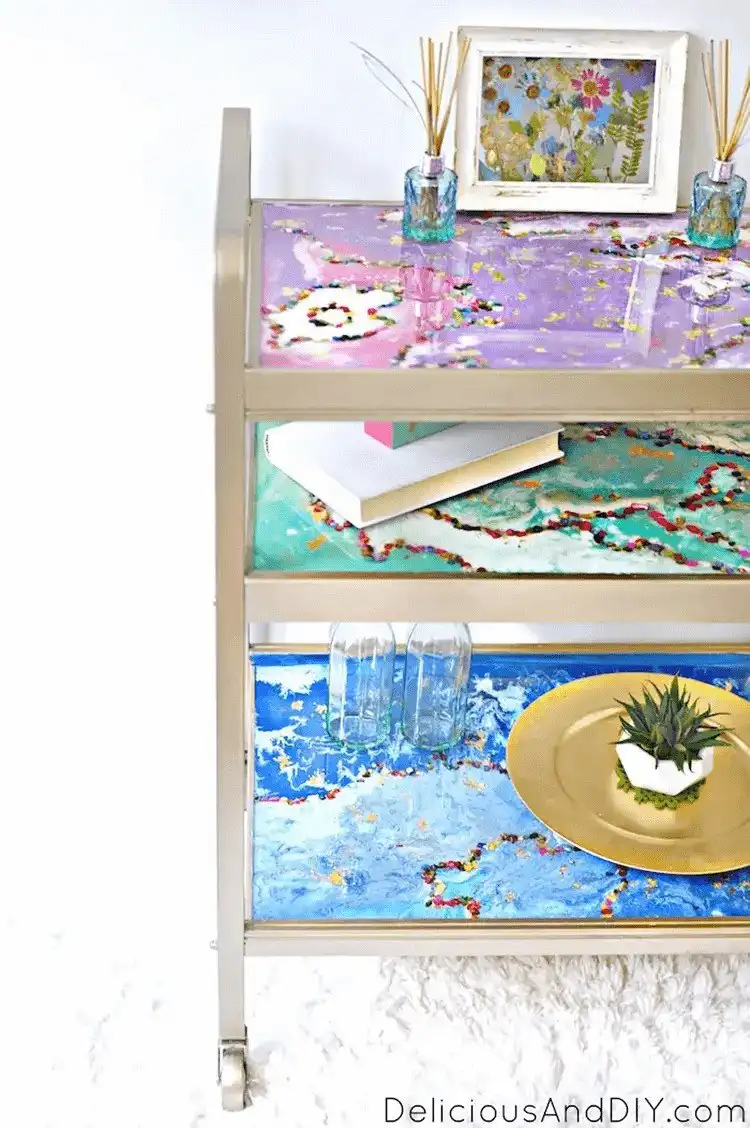 A modern bar cart with a glossy, custom-designed resin top featuring abstract patterns in white and gold.