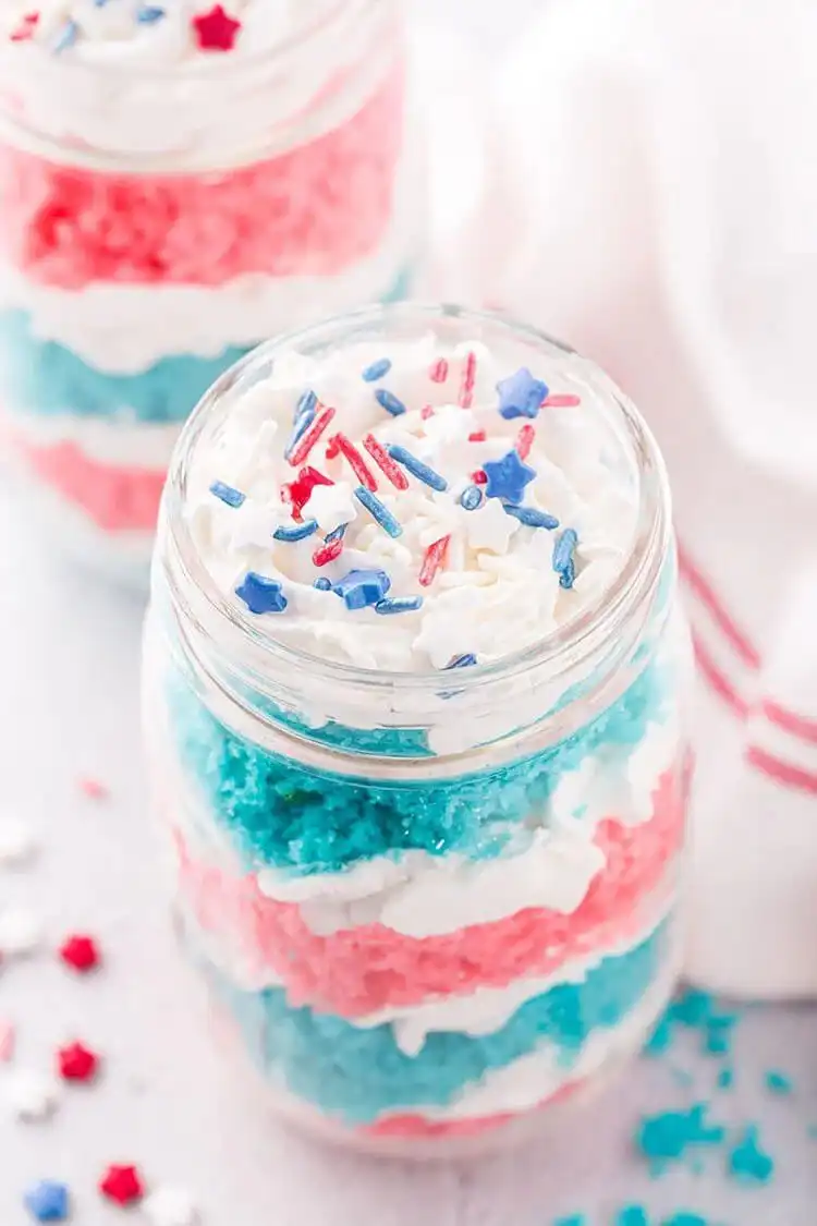 Fourth of July Cake in a Jar showing patriotic layers of white cake and whipped cream, topped with red, white, and blue sprinkles.