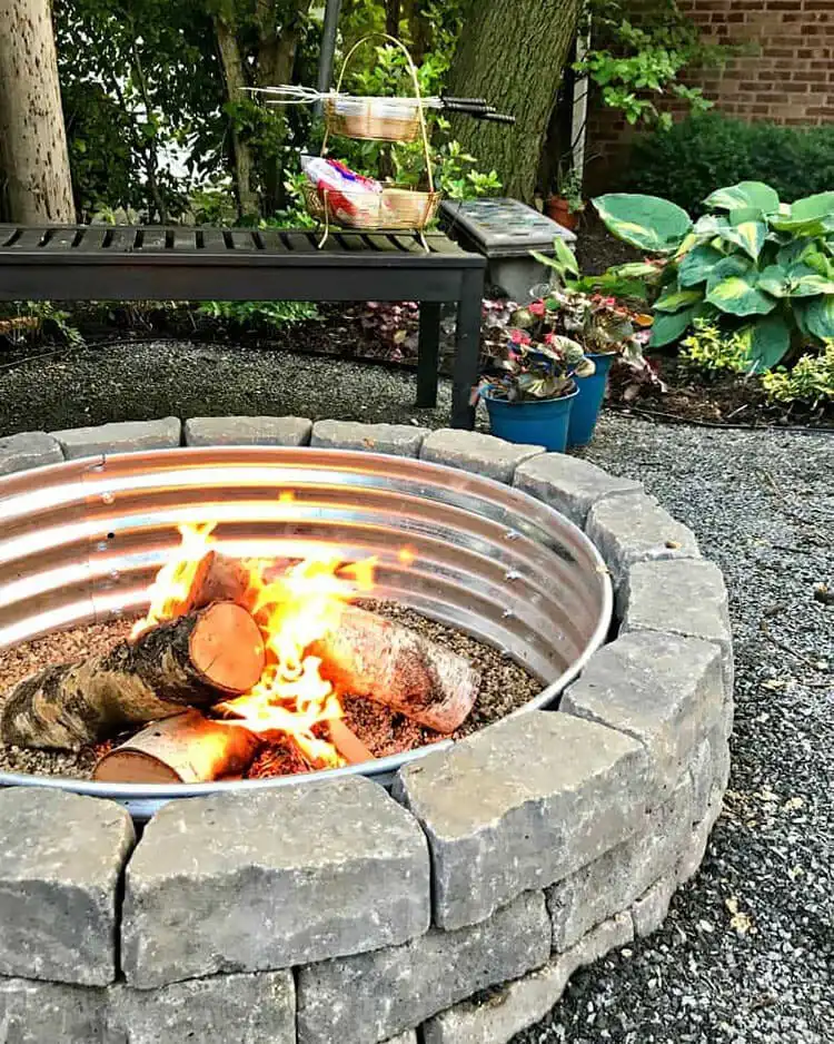 Classic How to Build a Backyard Fire Pit using grey segmental retaining wall blocks and a visible galvanized metal fire ring for durability.