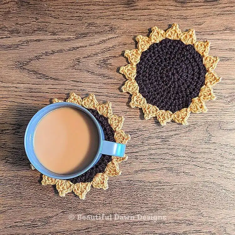 Yellow and brown crochet sunflower coaster next to a coffee cup