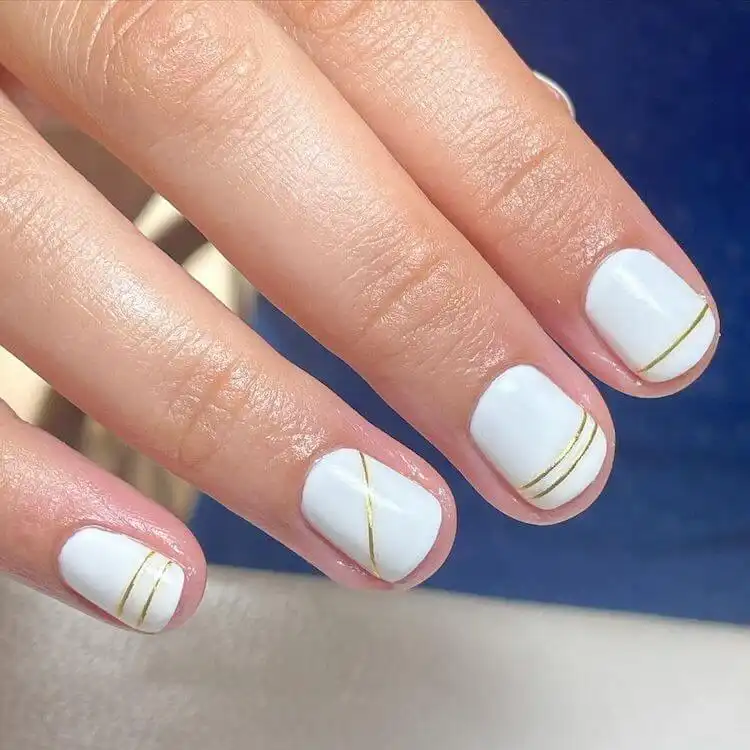 Simple white short acrylic nails with delicate gold lines in various directions.