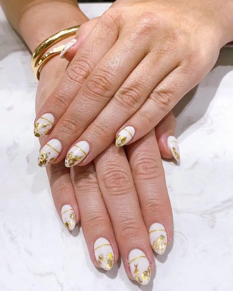 White nail polish covered with opulent gold flakes for a luxurious look.