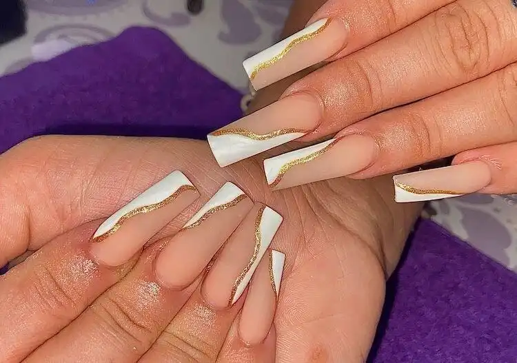 Short white and gold acrylic nails with a modern French tip and elegant gold swirl.