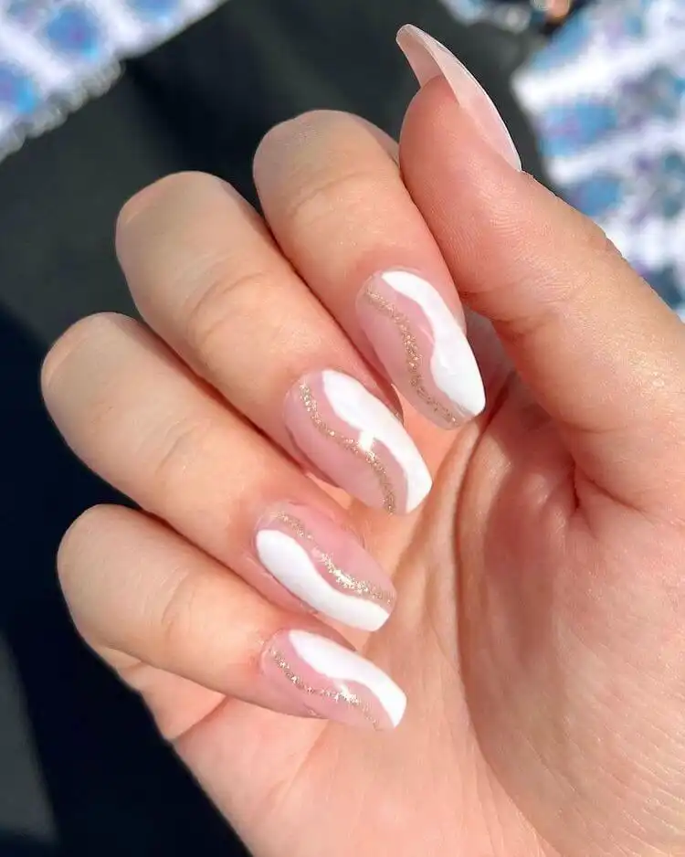 Dramatic stiletto nails featuring clear, white, and gold flakes with a diamond embellishment.