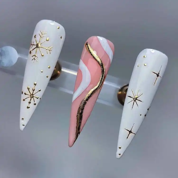 Festive white and gold Christmas nails with hints of pink on stiletto shape.
