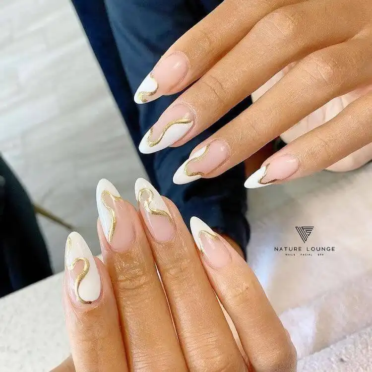 Almond-shaped white nails featuring intricate gold swirl patterns.