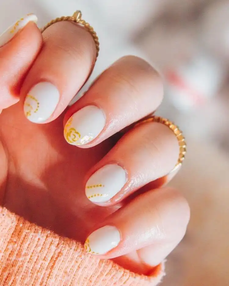 White short acrylic nails with subtle gold details like tiny flowers and dots.