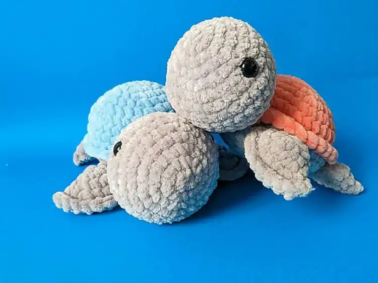A small amigurumi crochet turtle with colorful shell details and cute safety eyes, slightly larger than a mini.