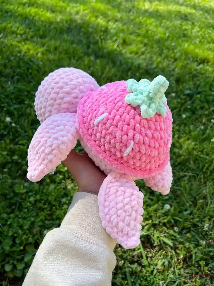An adorable crochet turtle featuring a red and green strawberry-themed shell, a whimsical and fruity design.