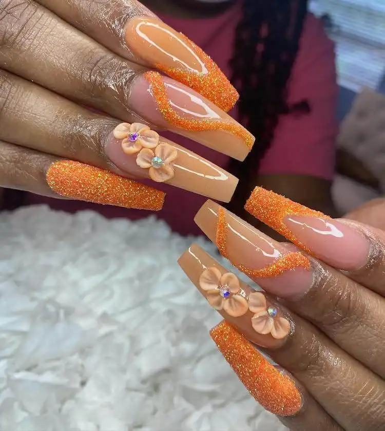 Orange glitter tapered square nails with delicate flower accents on the ring finger.