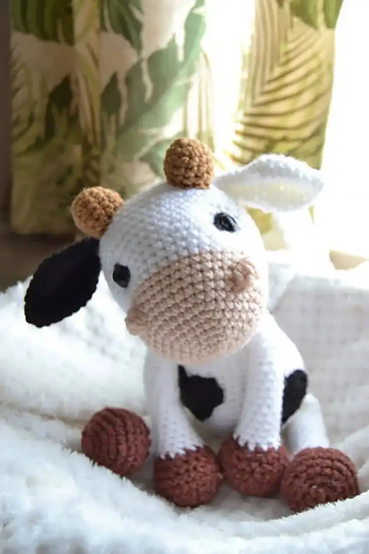 A tiny crochet cow holding a miniature milk bottle, designed as a cute keyring or small amigurumi decoration.