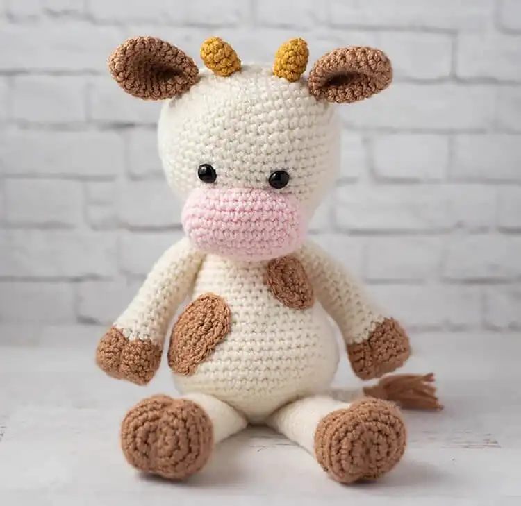 Penny the Cow, a tri-colored crochet plushie with distinct patches of white, black, and brown, depicting a classic farm cow.