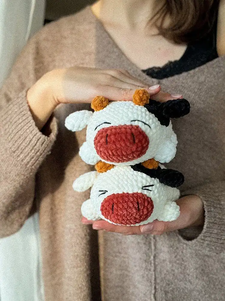 A round and squishy crochet Chubby Cow plushie in classic black and white, with an endearing smile.