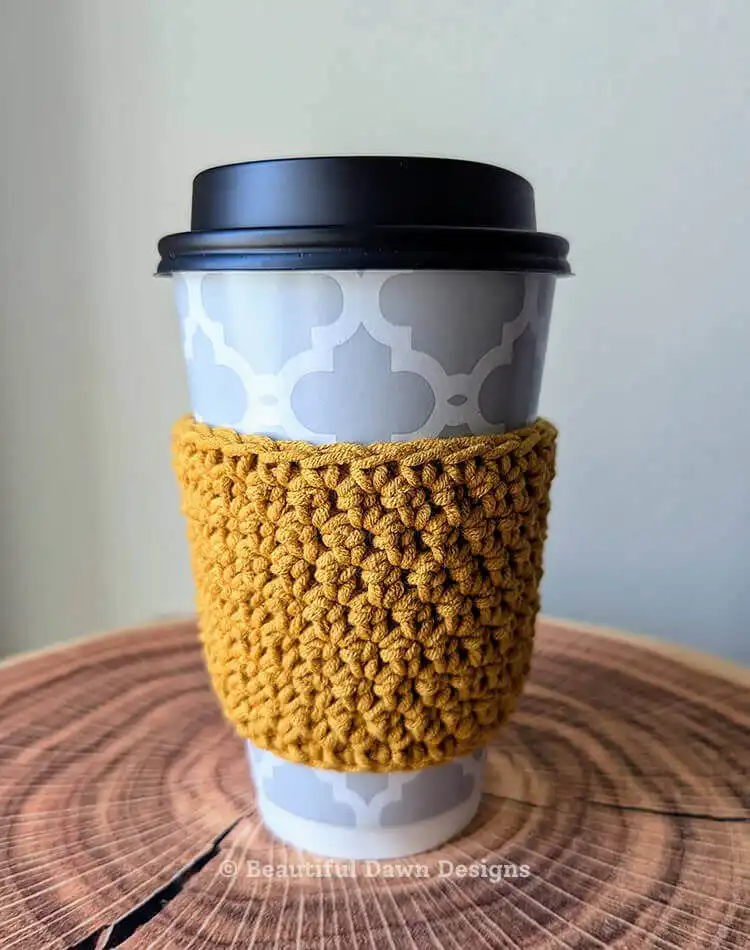 Close-up of a 20-Minute Crochet Cup Cozy in a bright yellow yarn, demonstrating how it fits a disposable coffee cup and highlighting the stitch detail.