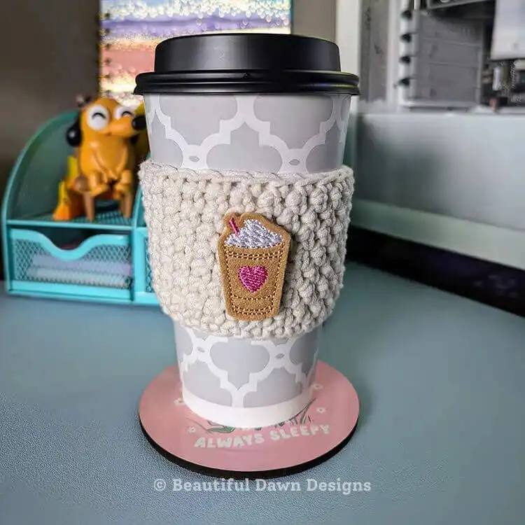 Various crochet tools including a hook, yarn, and stitch marker laid out on a surface, next to a finished 20-Minute Crochet Cup Cozy.