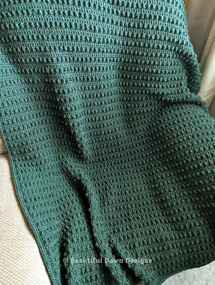 A folded, textured crochet blanket in a deep green color, named Evergreen Blanket