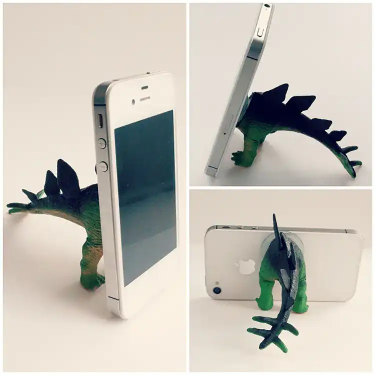 A plastic dinosaur toy painted and modified to securely hold an iPhone, serving as a quirky and functional tripod.