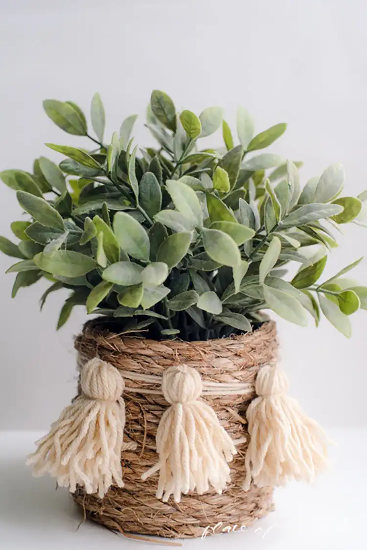 A cylindrical handmade rope basket with natural texture, holding a potted plant on a wooden surface.