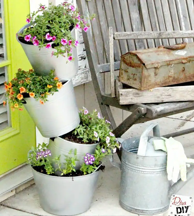 Plastic flower pots painted to mimic the look of galvanized metal, arranged with vibrant plants on a porch.