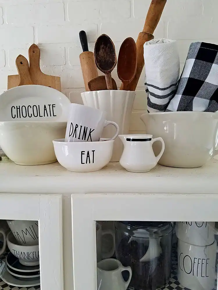 Dollar store mugs and bowls customized with Rae Dunn inspired lettering, arranged in a kitchen vignette.