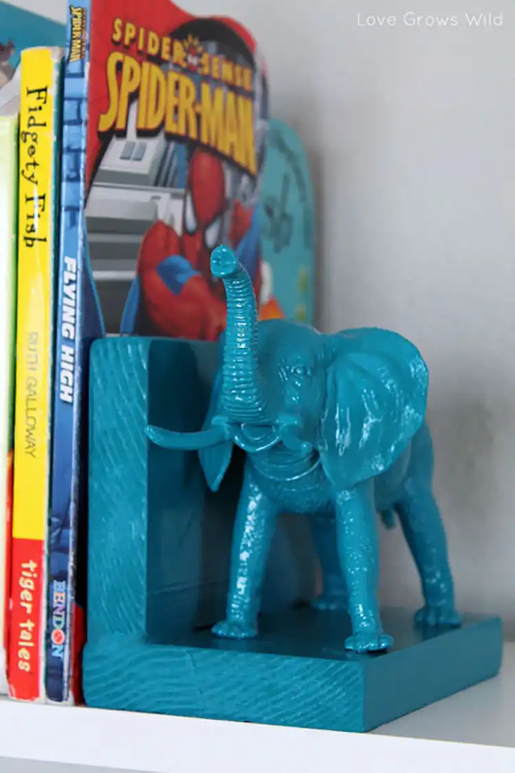 Two plastic elephant figurines painted in a matte color, repurposed as decorative and functional bookends on a bookshelf.