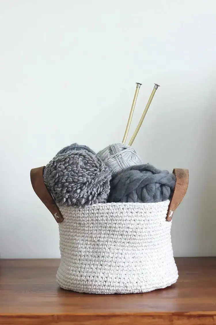 A rustic crochet basket made from dollar store twine and accented with a strip of a thrifted leather belt, holding small craft items.