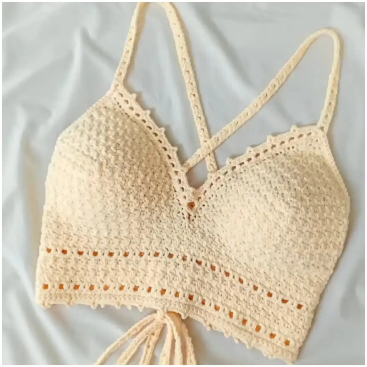 Front and back view of a cream crochet bralette with a V-neckline and lace-up detail, worn by a model