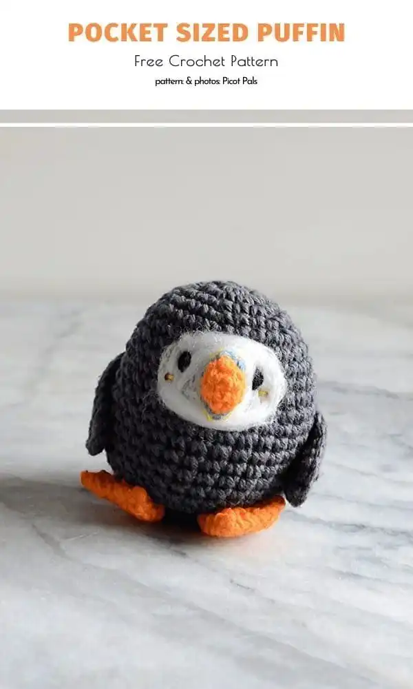 An adorably round, pocket-sized amigurumi puffin with dark grey body, orange beak, and light blue details.