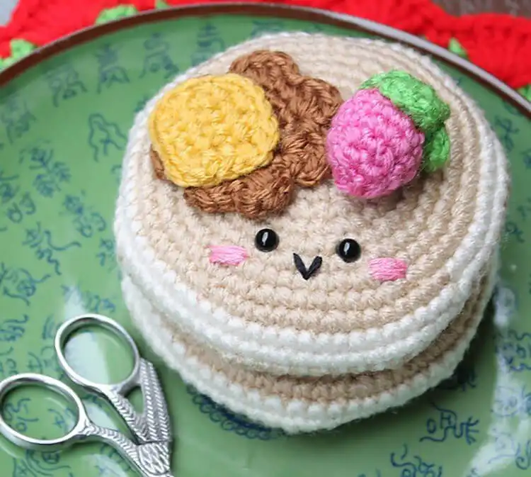 A stack of crocheted pancakes with a pat of butter, syrup drizzle, and a strawberry on top.