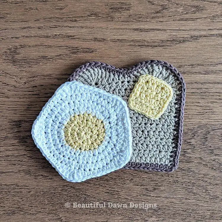 Two crocheted coasters, one shaped like buttered toast and the other like a fried egg.