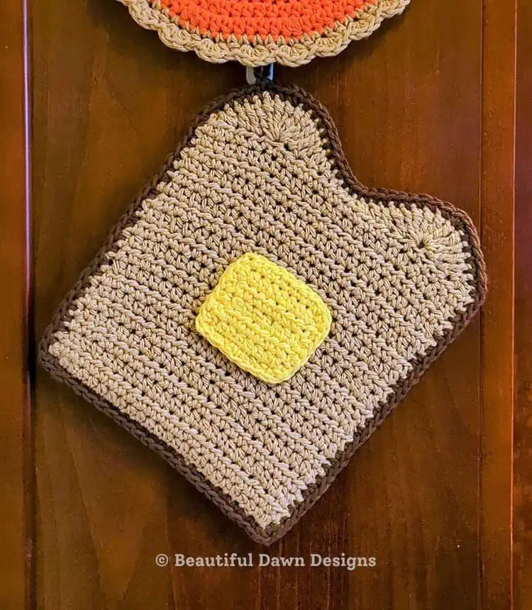 A charming crochet potholder designed to look like a slice of buttered toast.