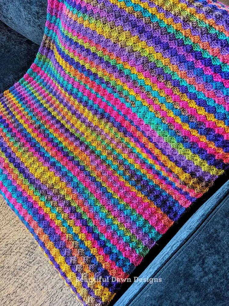 Comfortable Blooming Hues Crochet Blanket Pattern draped over a sofa, showcasing its practical use and aesthetic appeal in a home setting.