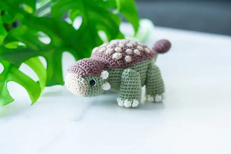 Crochet Ankylosaurus showcasing its distinctive armored plates and club-like tail, rendered in an earthy green color.