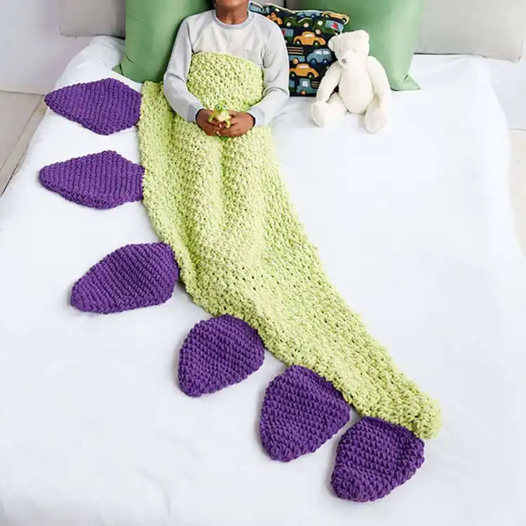 Cozy green crochet Dino Tail Snuggle Sack, designed for children to wear, featuring soft spikes along the back.