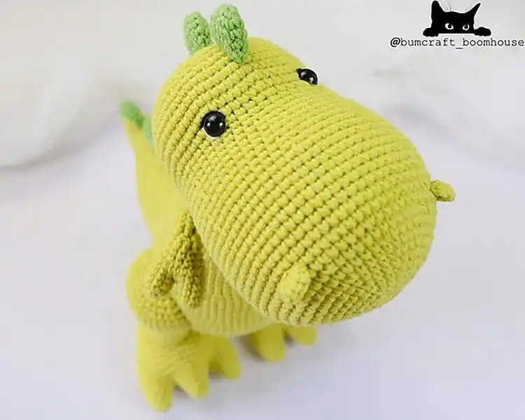 Friendly crochet T-Rex Dinosaur in contrasting green and beige, showing off its powerful legs and tiny arms.