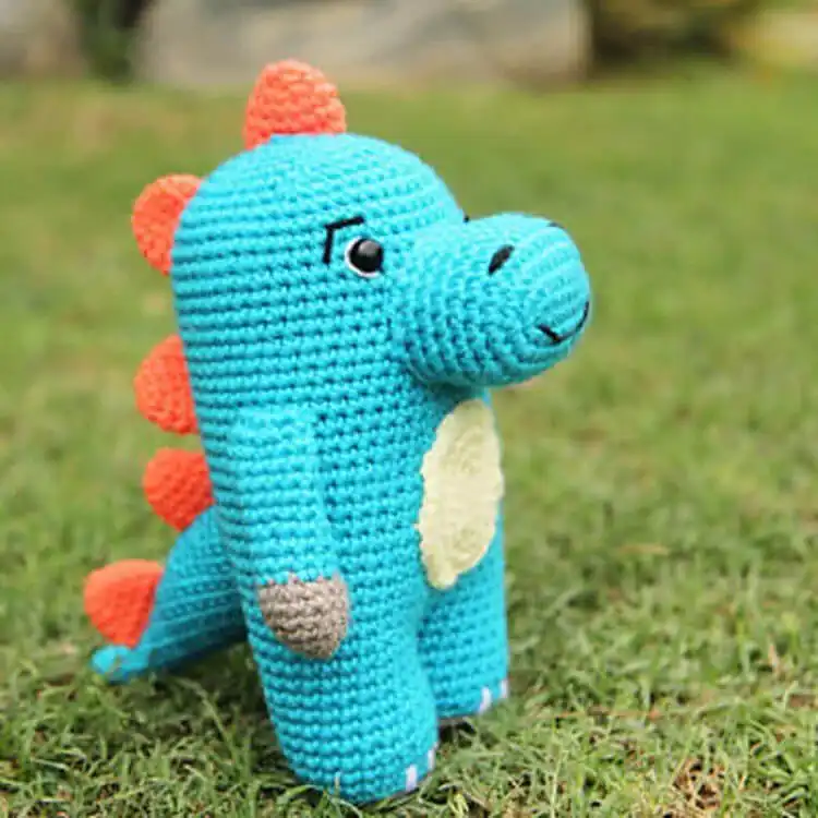 Endearing crochet Dewey the Dinosaur in a bright green hue, with small spikes and a lovable rounded shape, about 8 inches tall.