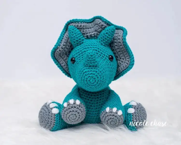 Detailed crochet Tanner the Triceratops, featuring distinct horns and a frill in contrasting colors, made with textured green yarn.