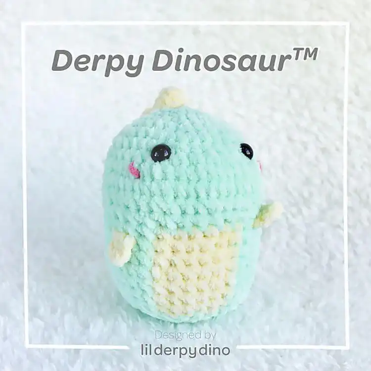 Small, charmingly imperfect crochet Derpy Dinosaur in bright yellow, with simplified features, perfect for beginner crocheters.