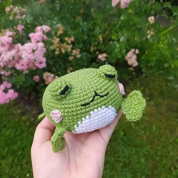 Classic green crochet Amigurumi Frog with white belly and large eyes, sitting on a wooden surface