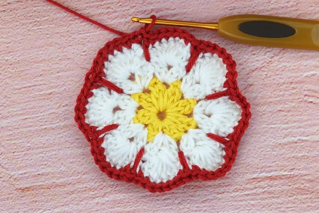 Photo tutorial of Round 4 in the African flower square crochet pattern, demonstrating the single crochet stitches and the unique long dc (spike stitch) technique, adding detail and finish.