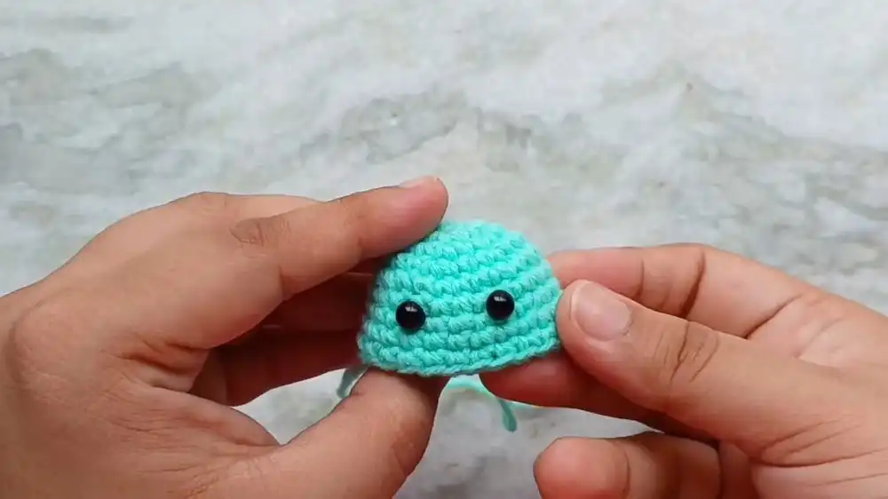 Crocheted jellyfish body with safety eyes inserted and beginning of shaping through decreases.