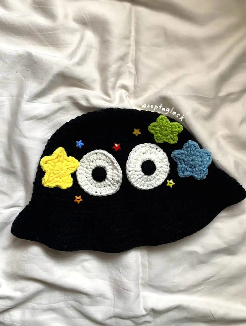 Cute Crochet Starry Bucket Hat with black base, vibrant yellow, green, and blue stars, and large cartoon eyes
