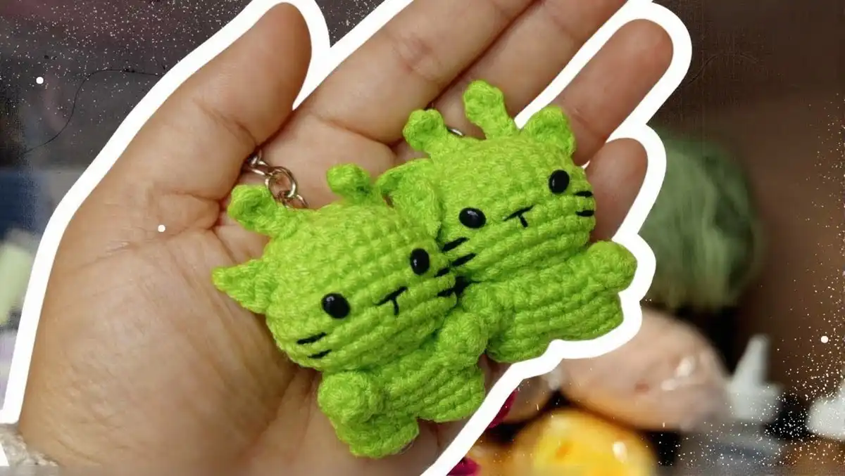 Cute finished Crochet Green Alien Cat Amigurumi Keychain Pattern, showing its green body, round head, safety eyes, embroidered whiskers, and small ears attached to a keychain ring.