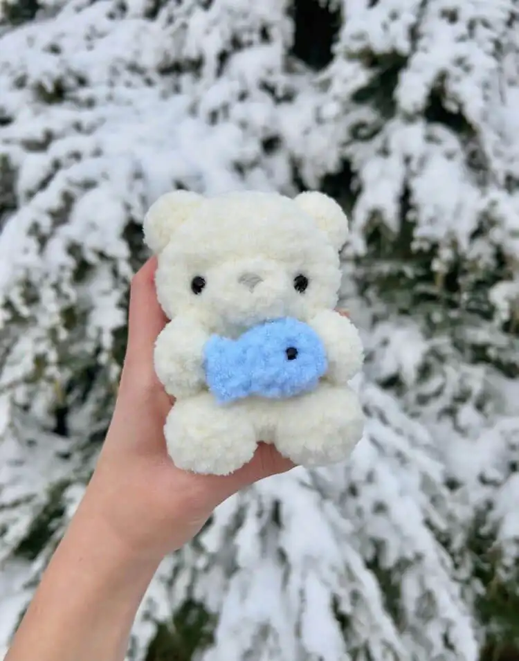 Cute white baby polar bear crochet plushie holding a small orange fish.