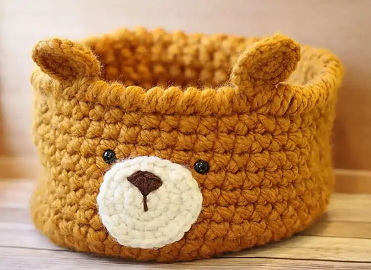 Crochet bear-shaped basket in beige yarn, with a cute bear face and ears.