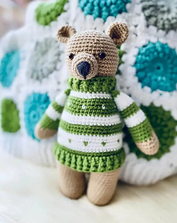 Small brown crochet teddy bear wearing a tiny blue and white striped pullover.