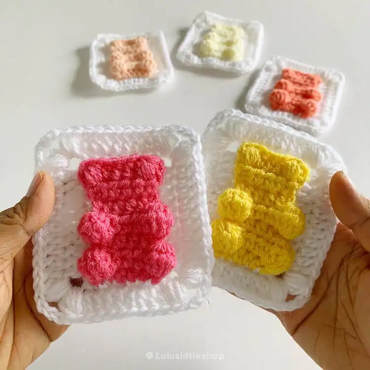 Crochet granny square featuring a pastel pink gummy bear design in the center.